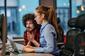 Business colleagues, a man and a woman, engage in discussing business strategies while attentively gazing at a computer monitor, epitomizing collaboration and innovation