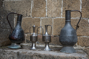 Antique metal vessels for water and wine. A copper jug in an ancient fortress. Antique handmade jugs made in the distant past. Traditional jugs of the Caucasus. Jugs for carrying water by women.