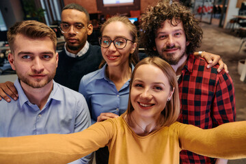 A diverse group of business professionals take a break from their tasks in a modern startup office to capture a creative selfie, showcasing teamwork and a vibrant workplace culture