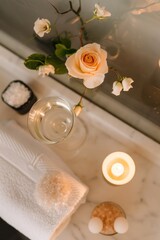 Top-view shot of a bath caddy with a glass of infused water, a single rose floating in a bowl, and a stack of bath salts beside a lit candle