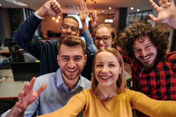 A diverse group of business professionals take a break from their tasks in a modern startup office to capture a creative selfie, showcasing teamwork and a vibrant workplace culture
