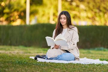 A woman is sitting on the grass reading a book