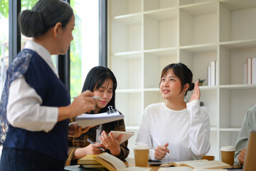 Pretty young woman student raising her hand to ask a question during class