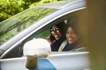 Two Muslim women wearing hijab converse on a smartphone while traveling together in a car through...