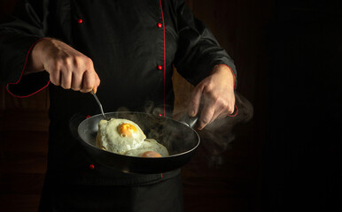 Experienced chef preparing scrambled eggs in the kitchen. The cook hand flips the egg on a steaming hot frying pan using a kitchen spatula. Concept of preparing a delicious breakfast with space for ad
