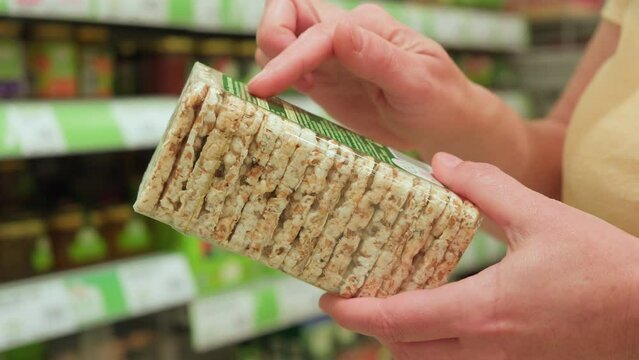 Vegan shopper reading label on bio organic rice crispbread in vegetarian section of supermarket.
