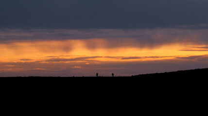 Silhouettes of three people, walking on top of a hill, golden hour sunset in the background and beautifully colored sky