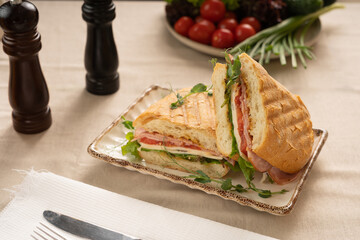 Two sandwiches with meat and cheese, lettuce and tomatoes between slices of grilled bread served on plate in restaurant or cafe