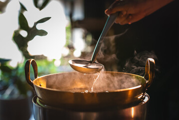 A brass pot is steaming while the chef cooks desserts using a ladle to stir in the brass pot.