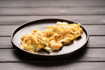 Italian pasta fettuccine in a creamy sauce with shrimps and parmesan cheese in black plate on table. Italian food