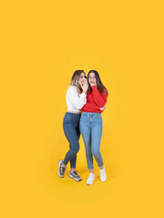 Whispering secrets, full body length caucasian best friends standing yellow studio background....