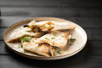 Hot lavash bread with melted suluguni cheese served on a white plate decorated with herbs.
