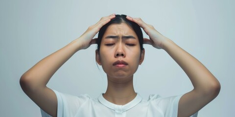 A young Asian woman is holding her head in pain