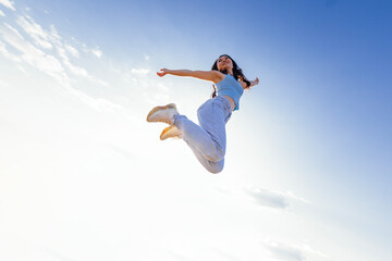 Charming Asian girl with long wave hair in casual clothes is jumping and laughing outdoors