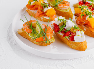 Elegant platter of assorted bruschetta with fresh toppings on a white background