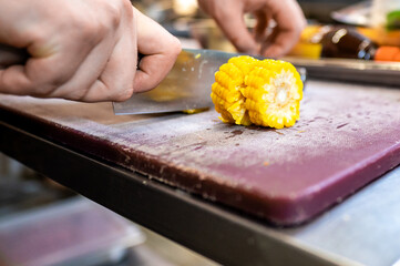 Close-up of hands slicing fresh yellow corn on a cutting board in a kitchen setting