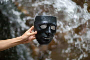 Selective focus black plastic mask in hand Waterfall nature background