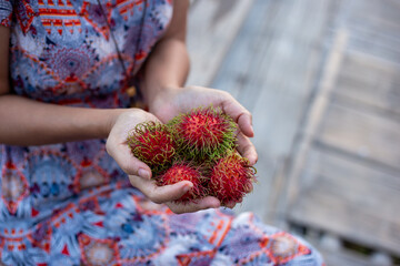 Selective focus red rambutan in young woman's hand Delicious fresh rambutan bought from the fresh fruit market. There is space for text.