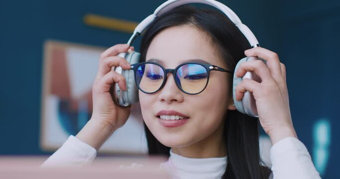 Young Asian girl enjoying good music while working or studying. Wearing big glasses for better vision. Charming woman following song beat by nodding her head. Relaxing morning for student.