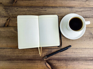 Coffee in a cup and a notebook with a pen on the table, top view.