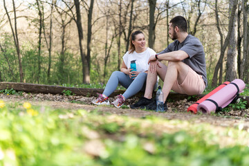 Fototapeta premium Sitting on a fallen tree trunk, the couple, including the determined overweight female, catch their breath, their laughter blending with the rustling leaves as they enjoy a post-workout moment. 