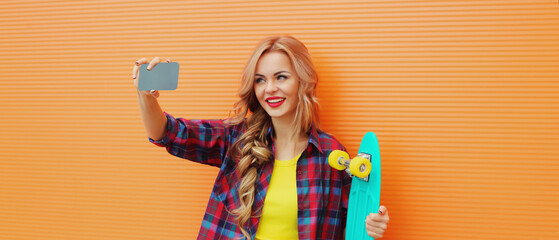 Summer portrait of happy smiling blonde young woman taking selfie with smartphone and skateboard