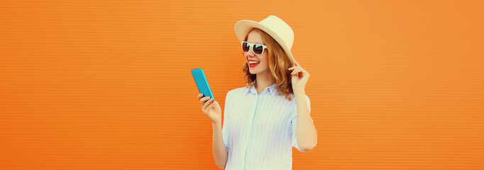 Summer portrait of happy young woman with mobile phone looking at device on orange background