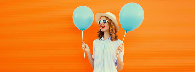 Portrait of happy smiling young woman with blue balloon wearing summer straw hat on orange