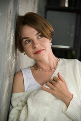 portrait of a beautiful smiling woman in white sweater staying near grey wall