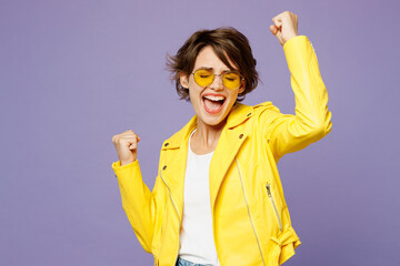 Young smiling woman wears yellow shirt white t-shirt casual clothes glasses doing winner gesture celebrate clenching fists say yes isolated on plain pastel light purple background. Lifestyle concept.