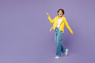 Full body side view young woman she wears yellow shirt white t-shirt casual clothes glasses walking going point index finger aside isolated on plain pastel purple background studio. Lifestyle concept.