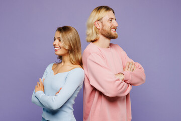 Sideways young couple two friends family man woman wear pink blue casual clothes together stand back to back hold hands crossed folded isolated on pastel plain light purple background studio portrait.