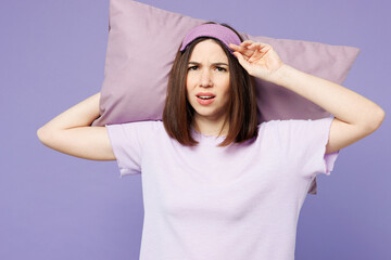 Young sad woman wearing pyjamas jam sleep eye mask rest relax at home hold pillow behind head look camera isolated on plain pastel light purple background studio portrait. Bad mood night nap concept.