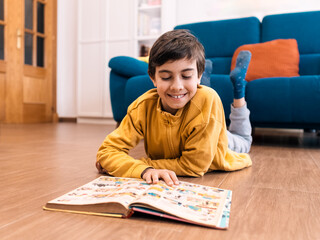 Young Child Engrossed in Reading a Colorful Book on Floor © javidestock