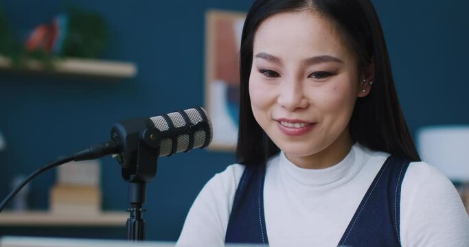Facial view of Chinese woman. Girl talking to microphone. Looking at script or screen in front of her. Recording blog or talking to followers. Popular streamer answering questions.
