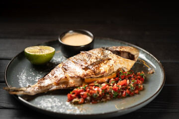 Grilled whole dorado fish served with vegetables, sauce and lemon on a blue plate. Seafood food