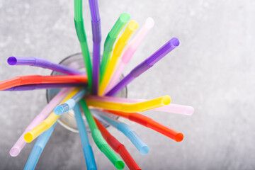 Colorful drinking straws in glass on grey background, closeup.