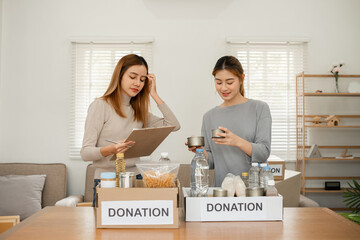 Two young female volunteers help pack food into donation boxes and prepare donation boxes to take...