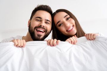 Photo of positive couple girl guy hold white blanket in bedroom smiling