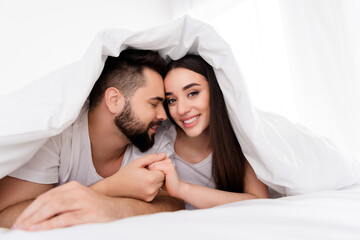 Photo of cheerful charming couple wear white t-shirts embracing indoors apartment bedroom