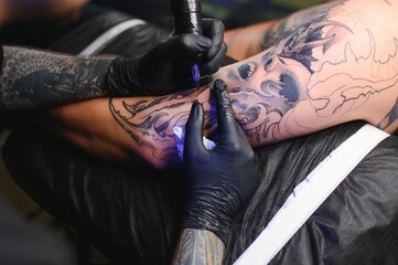 Male tattoo artist holding a tattoo gun, showing a process of making tattoos on a male tattooed...