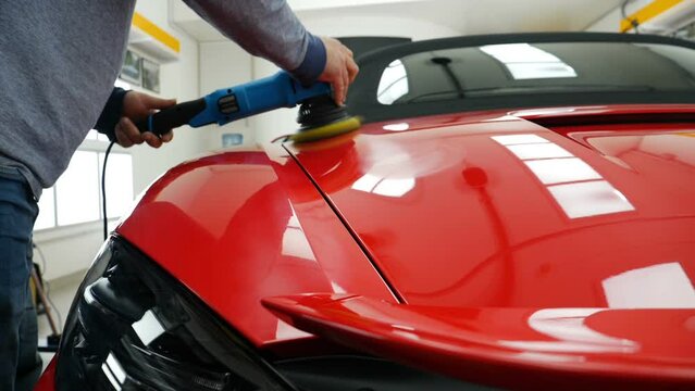 A man in a special suit polishes a gray car body, a tool for polishing cars, into a workshop.	
