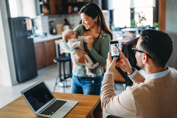 Proud father take picture of his wife with infant baby at home. Happy family, technology concept.