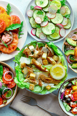 Fresh salads, overhead flat lay shot of an assortment. Variety of plates and bowls with green vegetables. Caesar salad with chicken and others