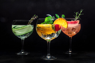 Fancy cocktails with fresh fruit. Gin and tonic drinks with ice at a party, on a black background. Alcohol with cucumber, orange, rosemary, mint