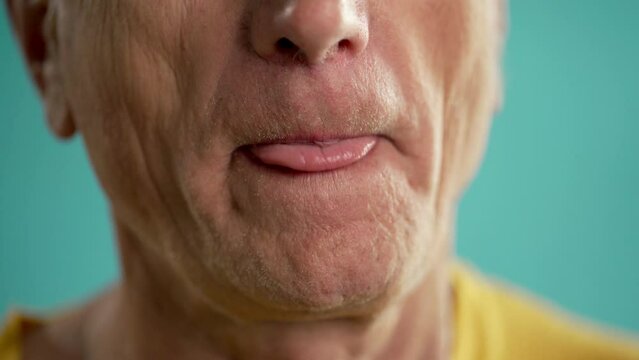 Close-up of old man licking his lips on blue background. Body parts