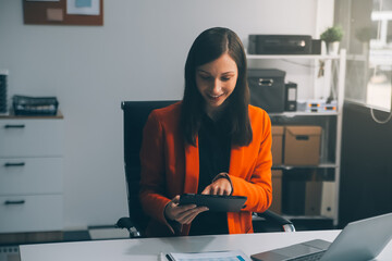 Smiling young Asian businesswoman working on a laptop computer at her desk in a bright modern home...