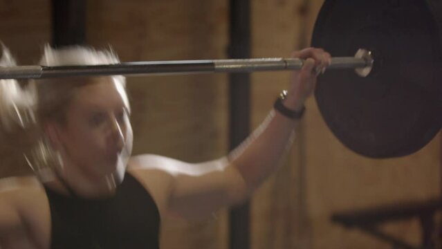 Powerful blonde girl does snatch weightlifting move with barbell, slomo