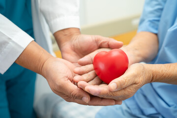 Doctor give red heart to Asian elderly woman patient in her hand on bed in hospital.