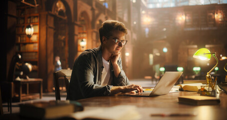 Focused Young Man Typing on Laptop in a Majestic Library, Illuminated by Soft, Warm Light,...